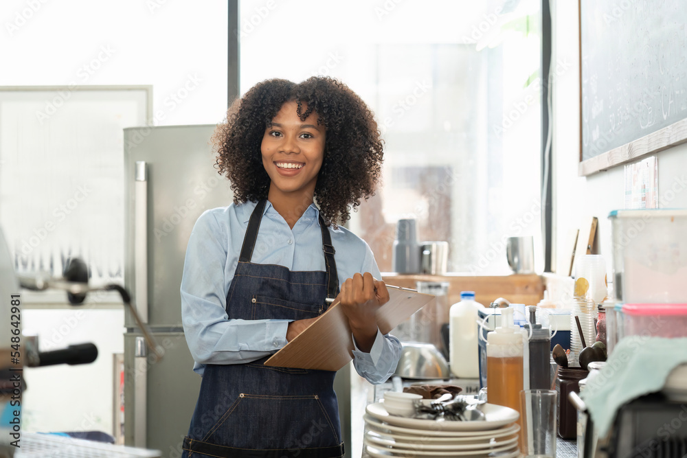 Portrait of a smiling young african american waitress wearing apron ready to take customer order