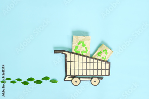 Environment friendly, sustainable, ecological shopping or consumerism and carbon footprint reduction concept. Shopping cart icon with fresh green leaves creative flat lay.