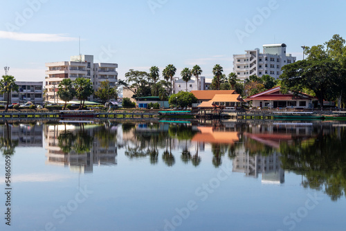 A view of the pier and bike path for exercise along the shores of the Nong Han River in Sakon Nakhon with reflecting buildings and houses.