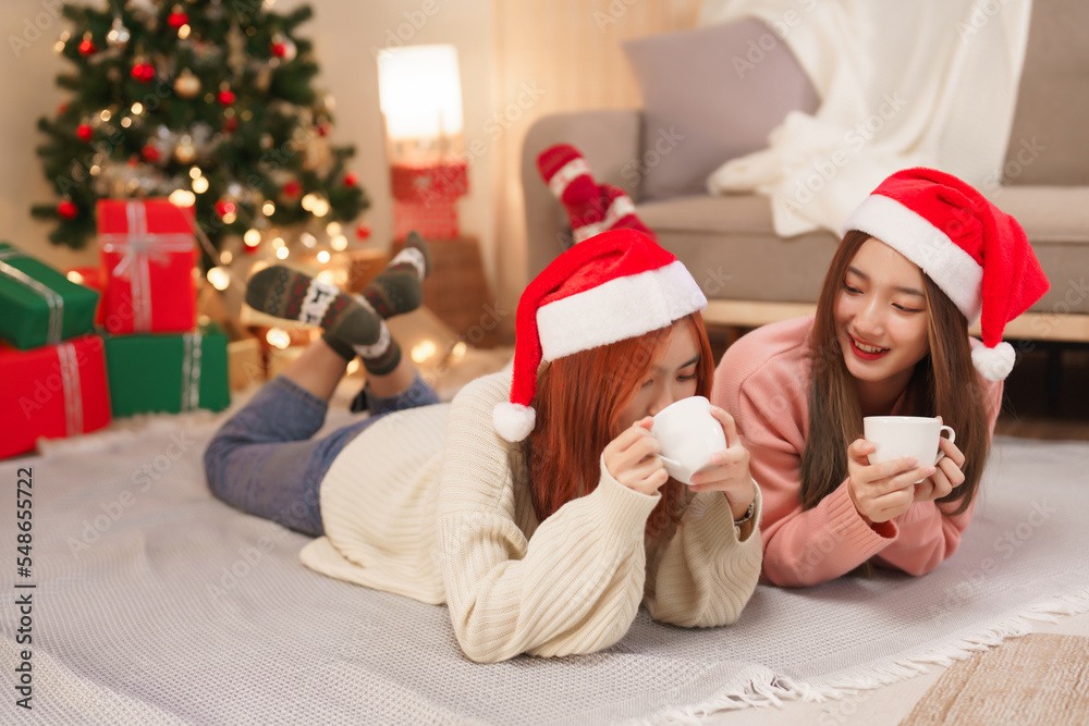 Christmas celebration concept, Two beautiful women in santa hat lying on floor and drinking coffee Christmas celebration concept, Two beautiful women in santa hat lying on floor and drinking coffee