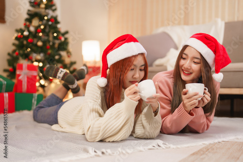 Christmas celebration concept, Two beautiful women in santa hat lying on floor and drinking coffee
