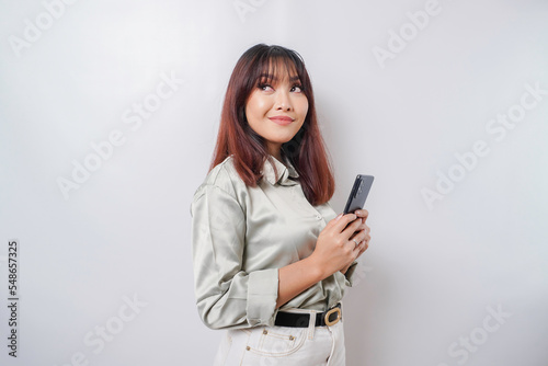 Photo of a thoughtful young woman holding her phone and looking aside; isolated on white color background