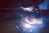 Close-up of male hands welding iron pieces, sparks and smoke Protection with welding gloves and masks caused by welding light.