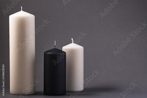 Two white candles and one black candle on a gray background.