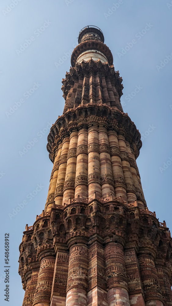 The world's tallest minaret of the ancient archaeological temple complex Qutb-Minar. The grandiose brick tower with balconies is decorated with carvings. The background is blue sky. Delhi. India