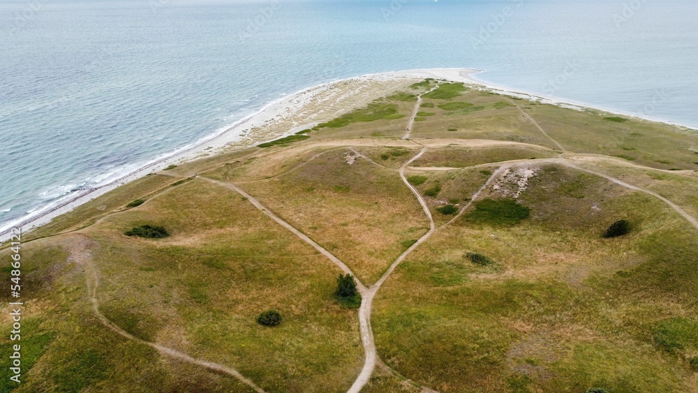Fototapeta premium High angle shot of sea waves crashing against the coast covered with green shrubs in Samso, Denmark