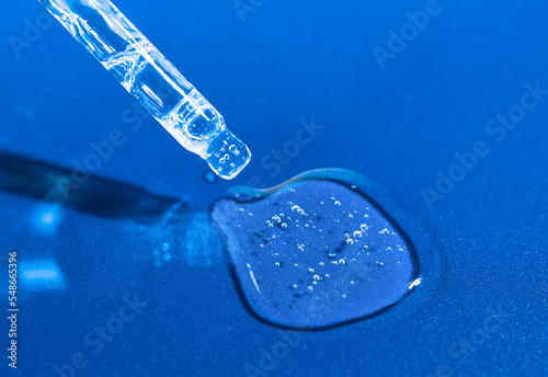 Glass pipette with transparent serum, hyaluron on a bright blue background. Body care product, moisturizing and nourishing the skin. © Юлия Черкасова