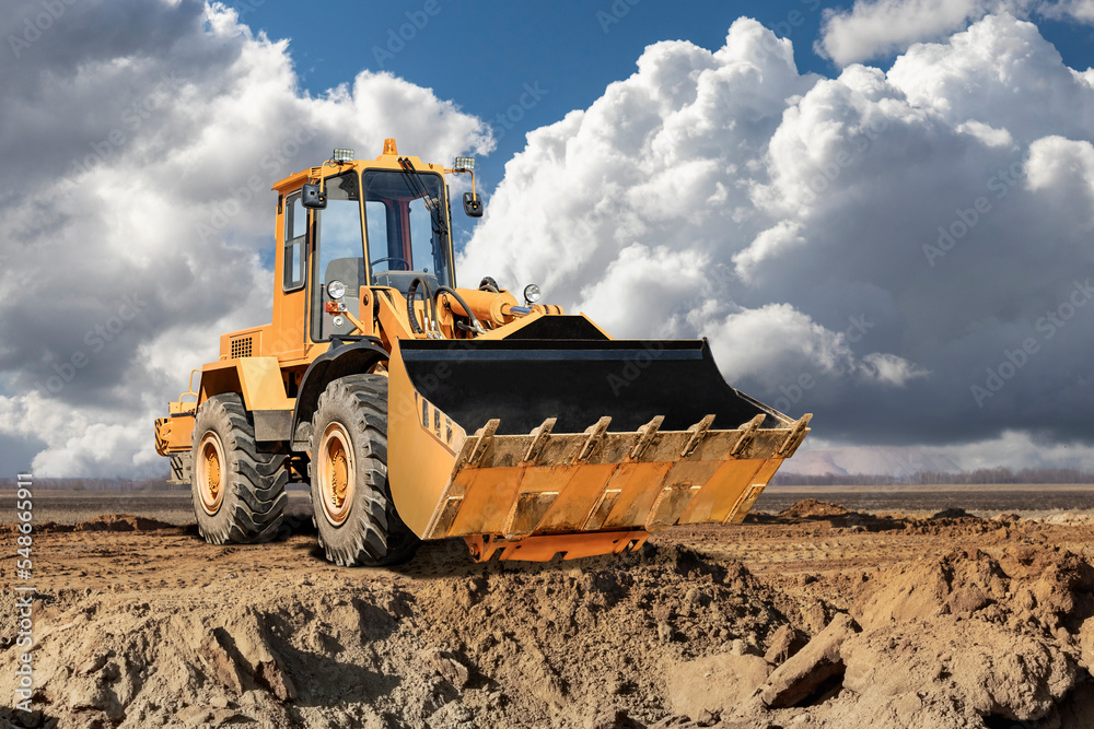 Bulldozer or loader against a cloudy sky. An earthmoving machine is leveling the site. Construction equipment for earthworks. Excavation of a pit for construction work. Bulldozer or loader against a cloudy sky. An earthmoving machine is leveling the site. Construction equipment for earthworks. Excavation of a pit for construction work.
