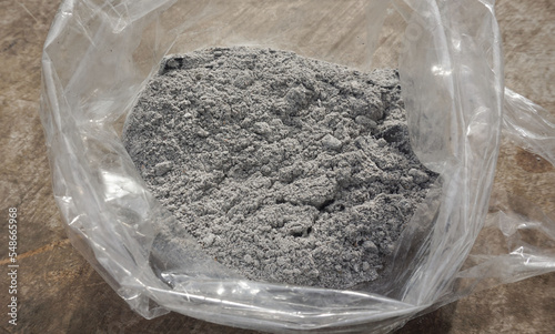 Gray ashes in a plastic bag placed on a wooden floor for use as a fertilizer for plants growing in an agricultural garden.