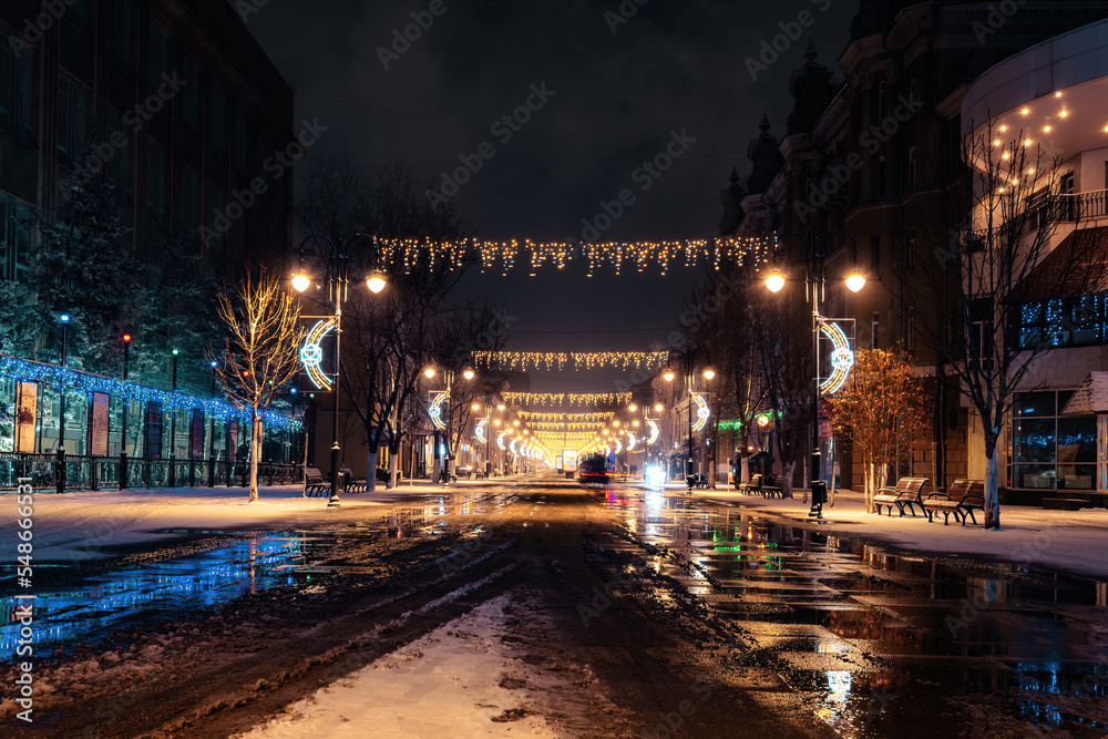 winter night on christmas decoration lighting street of town during melted snowfall precipitation