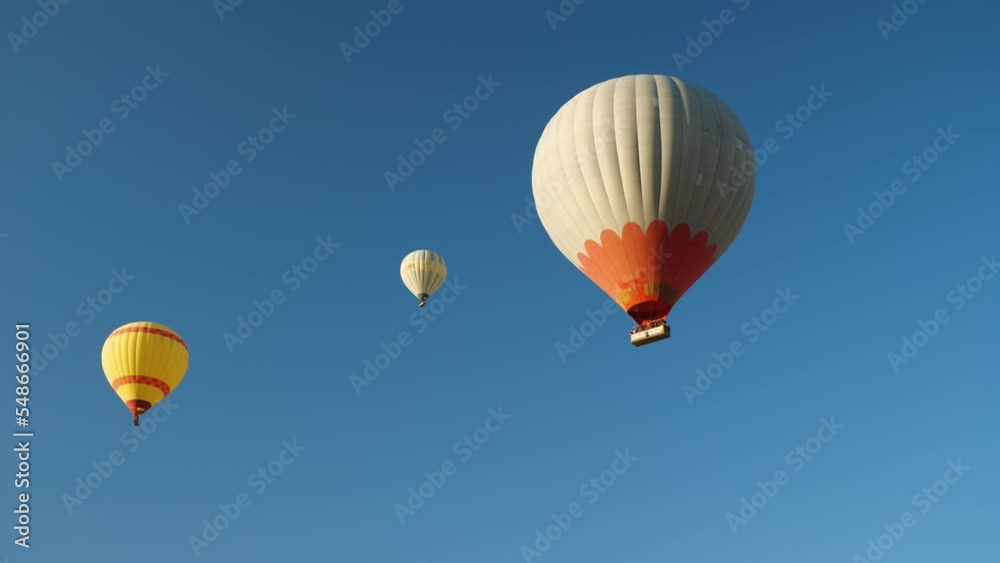Three hot air balloons with tourists in the background of a blue cloudless sky. Beautiful view of multicolored Hot air balloons from below Three hot air balloons with tourists in the background of a blue cloudless sky. Beautiful view of multicolored Hot air balloons from below