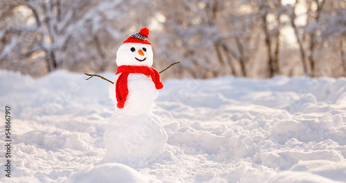 Snowman in red knitted hat and scarf with carrot nose and joyful smile in snowy winter park