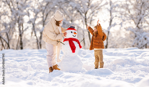 Foto Cute little boy making snowman with mom in winter park