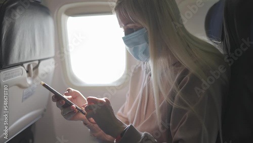 an emigrant woman in an airplane seat watching the news on her phone