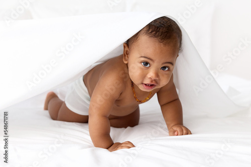 Baby boy on all fours hiding under white sheet photo