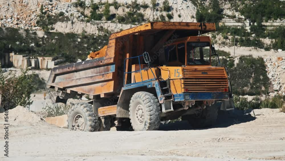 Unrecognizable man working in marble quarry driving haul truck transporting ground and stones on sunny summer day Unrecognizable man working in marble quarry driving haul truck transporting ground and stones on sunny summer day