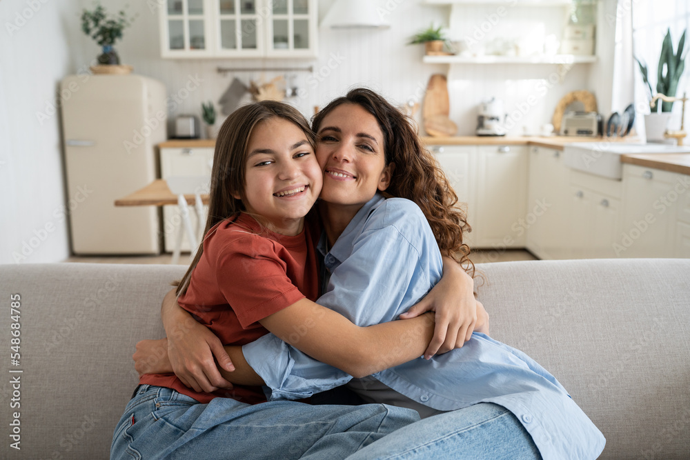 Portrait of happy Caucasian family single mother and teenage daughter hugging cuddling, spending time together at home, looking at camera and smiling. Mother-daughter friendship, positive parenting