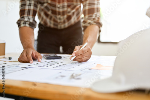 Asian male engineer or architect checking building scale, working on his blueprint in the office.