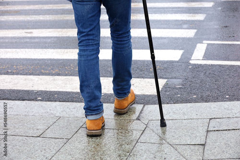Man walking with a cane on crosswalk. Male legs in jeans on pedestrian crossing, street safety