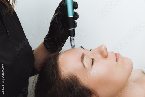 Cosmetic mesotherapy for facial rejuvenation. Cosmetic procedure of microneedling. The cosmetologist injects hyaluronic acid into the face of the girl's patient with the help of dermopen.