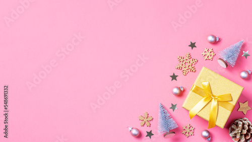 Christmas golden gift box with mini Christmas trees and baubles on pastel pink background