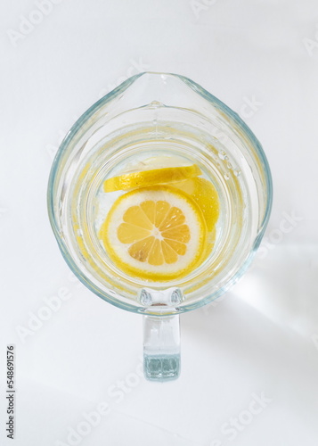 Natural lemonade in a glass jug on a white background close-up. Sliced lemons in clear water and the glare from the sun ray. Overhead view.