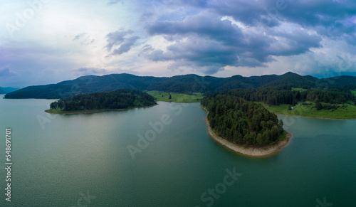 Lake covered with vegetation against backdrop of Rhodope mountains and clouds. Panorama, top view