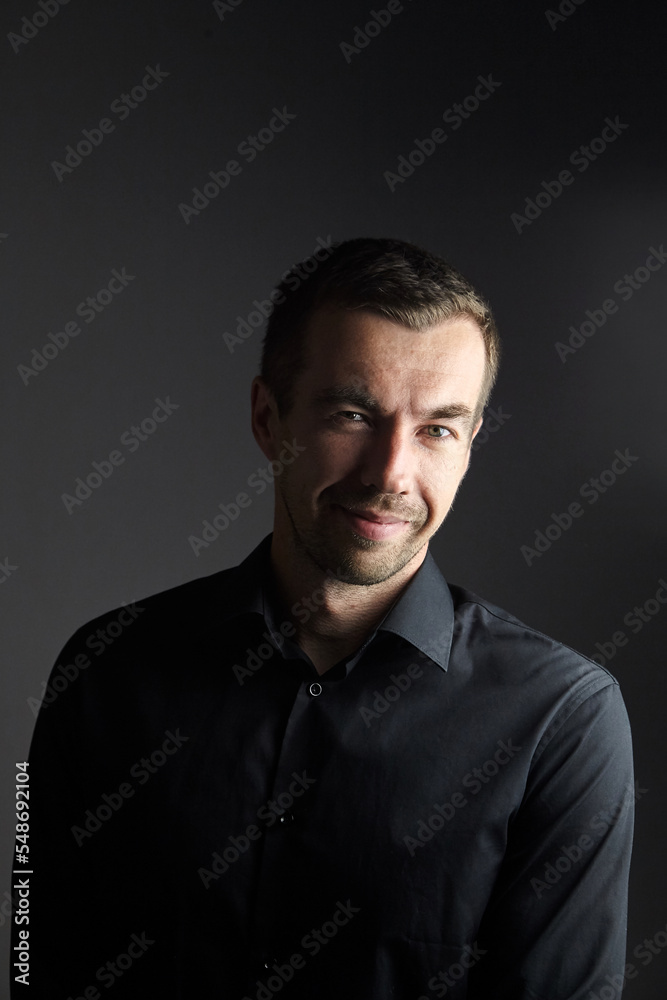 Portrait of smiling man in a black shirt on a dark background. Portrait of young caucasian man Portrait of smiling man in a black shirt on a dark background. Portrait of young caucasian man