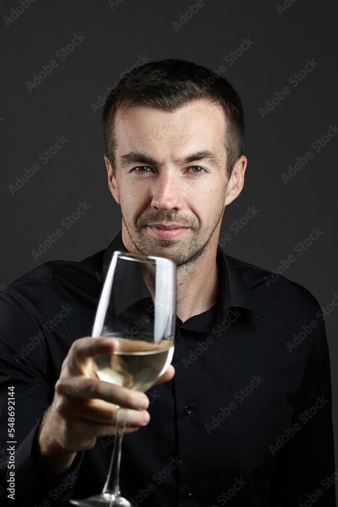 Portrait of smiling man in a black shirt with wine glass in hand on dark background. Portrait of young caucasian dark-haired man Portrait of smiling man in a black shirt with wine glass in hand on dark background. Portrait of young caucasian dark-haired man