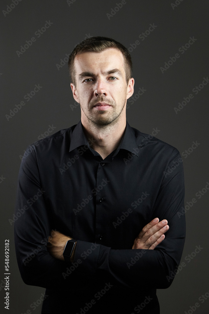 Portrait of man in a black shirt on a dark background. Serious brunet with arms folded. Young caucasian man