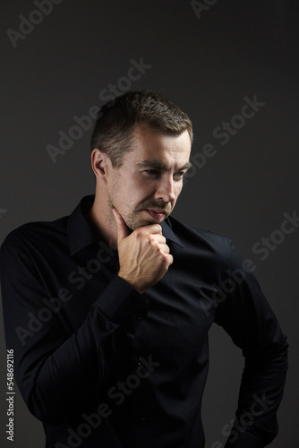 Portrait of pensive man in a black shirt on a dark background. Young caucasian dark-haired man