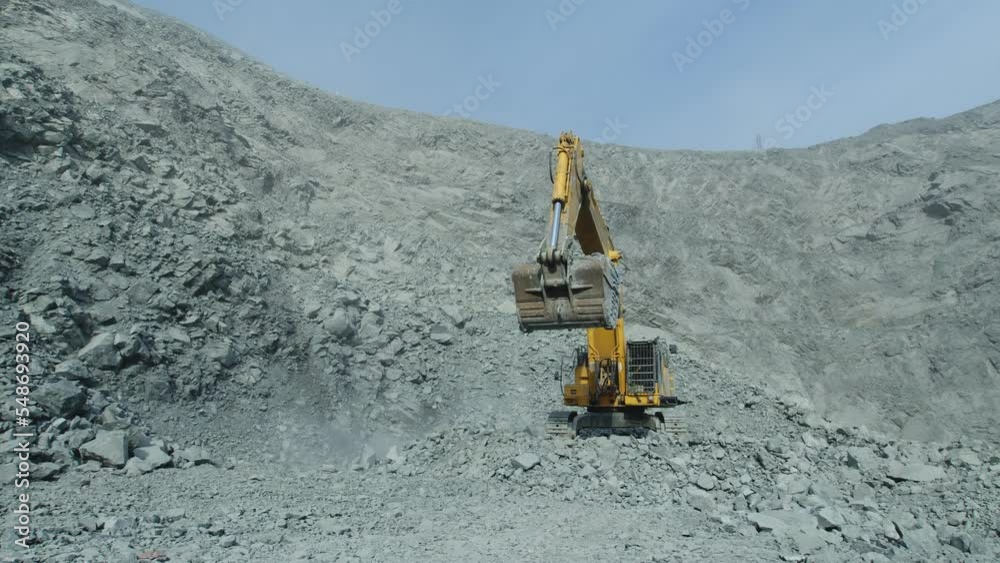 Yellow excavator picking up a full bucket of ore at a work site in dusty quarry. Heavy mining excavator preparing to loading rocks at opencast mine Yellow excavator picking up a full bucket of ore at a work site in dusty quarry. Heavy mining excavator preparing to loading rocks at opencast mine