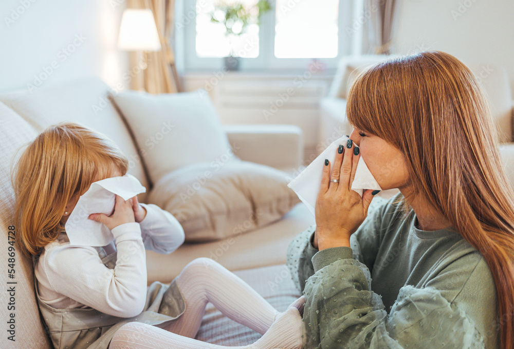 Young mother showing her small girl the right way to blow a nose. Little girl blowing nose while being with her mother at home. Adorable girl blowing nose into tissue paper by his mother at home. Young mother showing her small girl the right way to blow a nose. Little girl blowing nose while being with her mother at home. Adorable girl blowing nose into tissue paper by his mother at home.