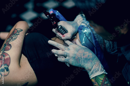 Professional tattooist makes the tattoo on a girl waist, focusing on tattoo machines in a modern studio lowlight.