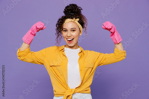 Young woman wear yellow shirt rubber gloves while do housework tidy up show hand biceps muscles demonstrate strength power isolated on plain pastel light purple background studio Housekeeping concept