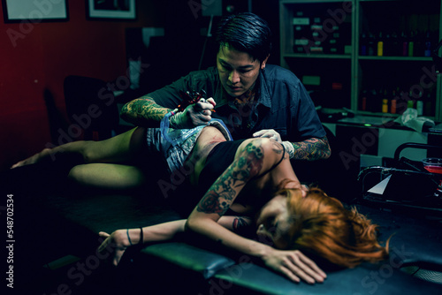 Professional tattooist makes the tattoo on a girl waist  focusing on tattoo machines in a modern studio lowlight.