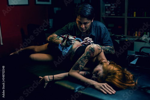 Professional tattooist makes the tattoo on a girl waist  focusing on tattoo machines in a modern studio lowlight.