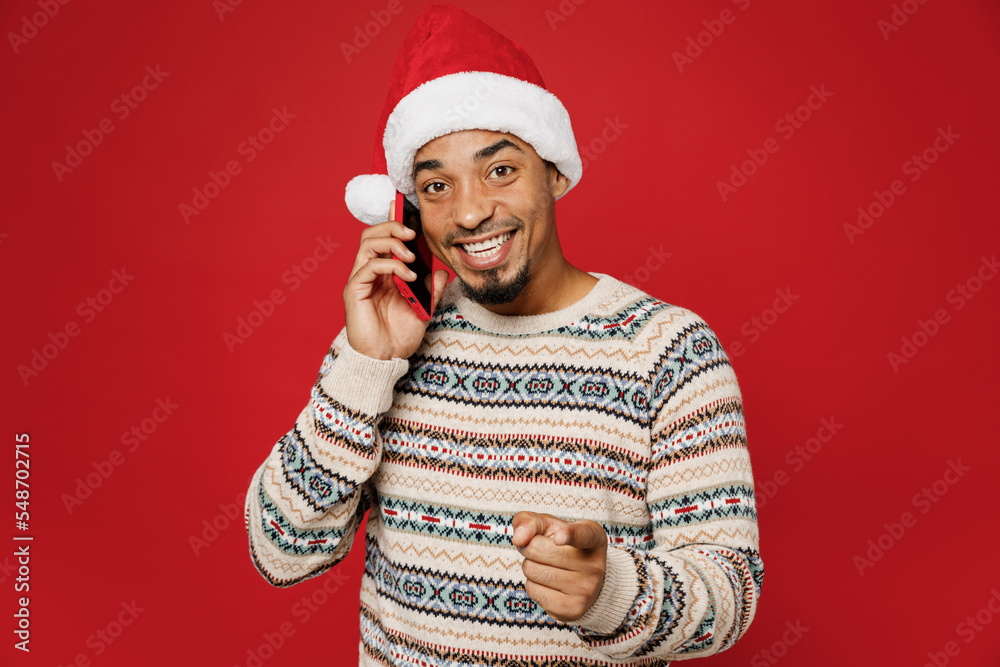 Merry young man wear warm cozy Christmas sweater Santa hat posing hold in  hand use mobile