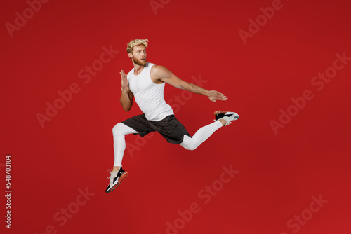 Full body side profile view young strong sporty toned sportsman man wear white clothes spend time in home gym run jump high look aside isolated on plain red background Workout sport fit body concept.