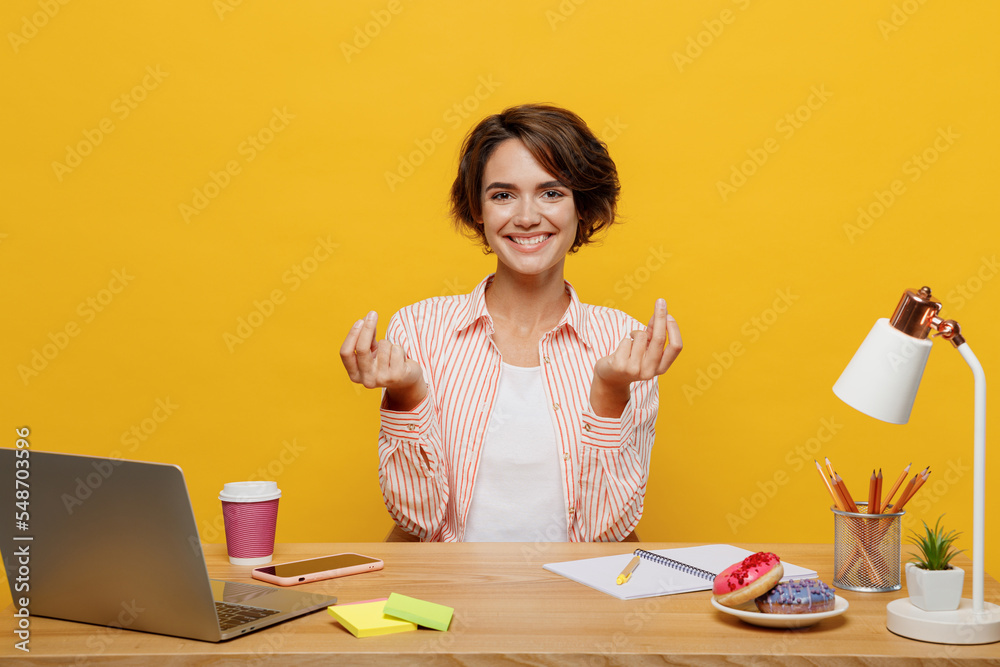 Young employee business woman in casual shirt sit work at office desk with pc laptop rub fingers show cash gesture ask for money isolated on plain yellow color background. Achievement career concept Young employee business woman in casual shirt sit work at office desk with pc laptop rub fingers show cash gesture ask for money isolated on plain yellow color background. Achievement career concept