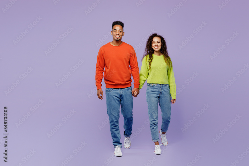 Full body smiling fun young couple two friend family man woman of African American ethnicity wear casual clothes hold hands walk go strolling together isolated on pastel plain light purple background
