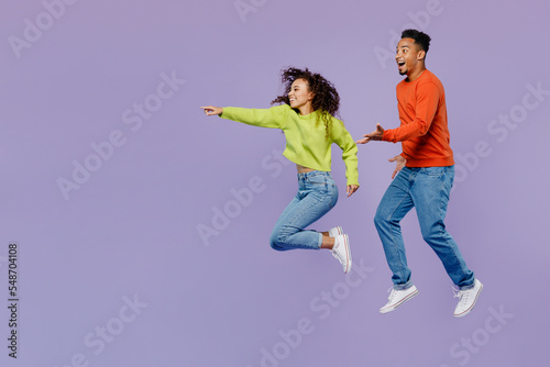 Full body side view young couple two friends family man woman of African American ethnicity wear casual clothes together point index finger aside on area isolated on pastel plain purple background.