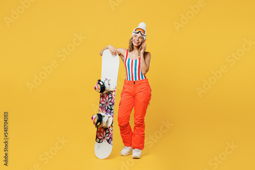 Snowboarder woman in orange suit goggles mask hat ski costume swimsuit spend extreme weekend talk speak on mobile cell phone isolated on plain yellow background Winter sport hobby trip relax concept © ViDi Studio
