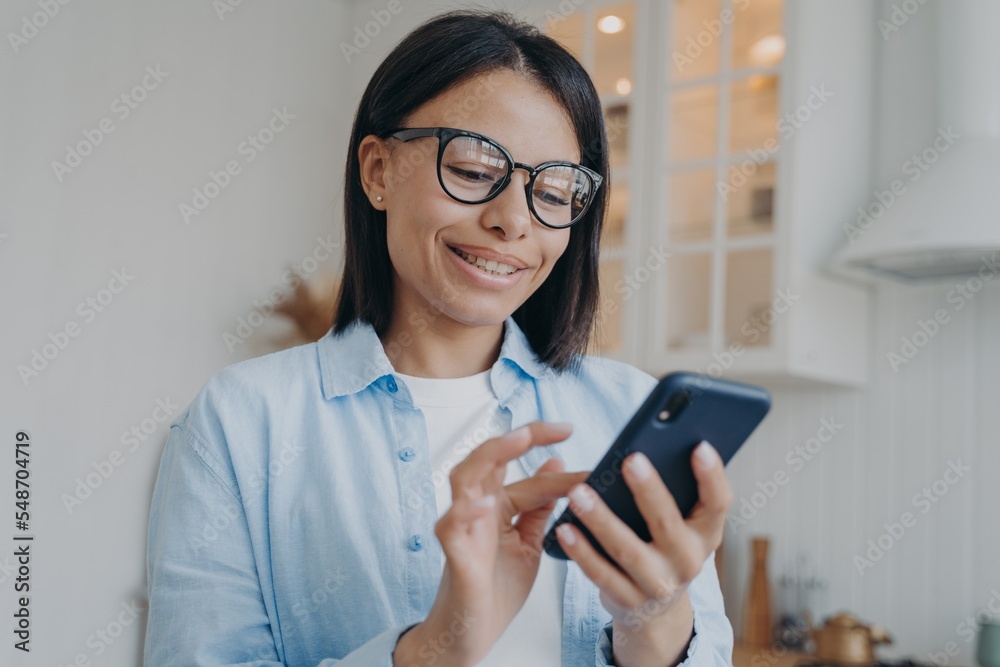 Mobile apps. Smiling female in glasses holding smartphone, shopping, using online services at home