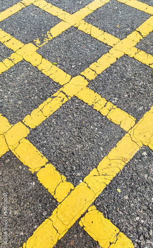 No parking area sign on the asphaltic surface, Yellow crossing sign on the textured floor, Yellow logo on grey color background