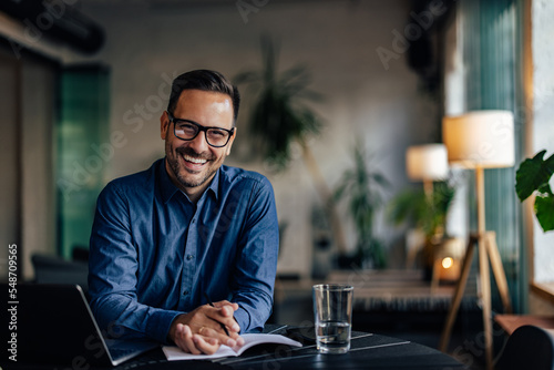 Happy male boss looking and smiling at the camera, being at the workplace. photo