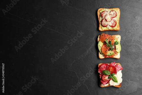 Tasty toasts with different toppings on black table, flat lay. Space for text