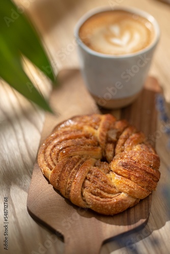 Vertical shot of a kringle pastry served on a wooden board with a cup of latte in the background