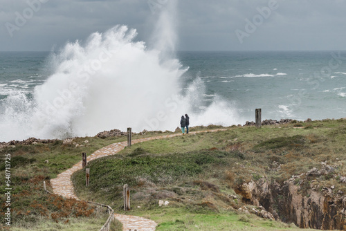 People watching the huge waves crashing on a breakwater. Weather alert on the coast with strong wind and large waves.