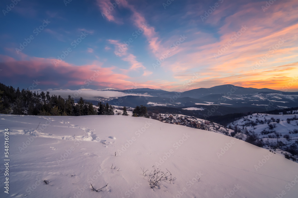 Beautiful sunrise view with snowy mountain slopes and small village among them in the frozen winter morning, the Rhodopi Mountains, Bulgaria .